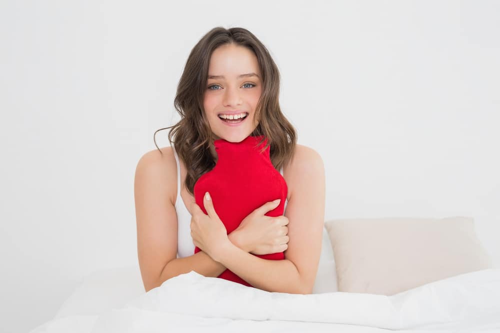 A woman holding a red hot water bottle in bed.