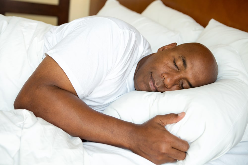 A black man resting peacefully in a white bed.