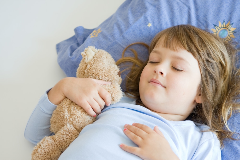 A little girl sleeping with a teddy bear.
