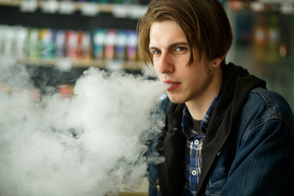 A young man smoking an e-cigarette in a store, seeking dental advice from Dr. Sean Endsley, a cosmetic dentist in Waco.