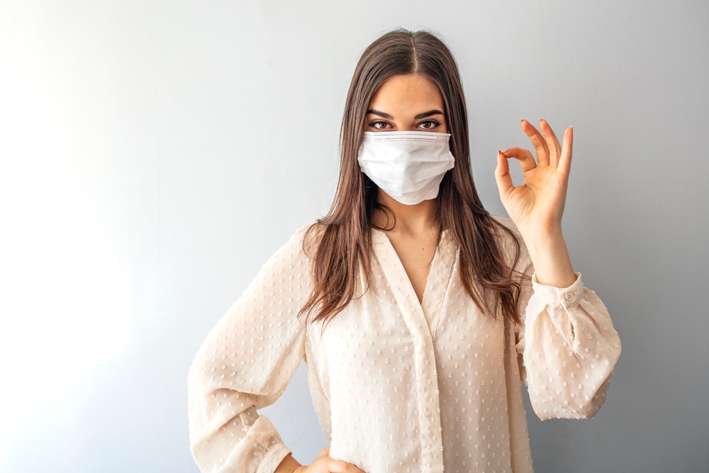 A young woman wearing a surgical mask and making an ok gesture at her general dentist, Dr. Sean Endsley.