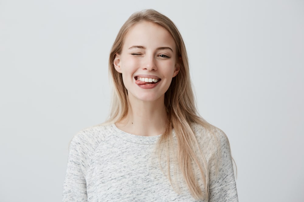 A young woman is laughing against a white background while surrounded by dental instruments.