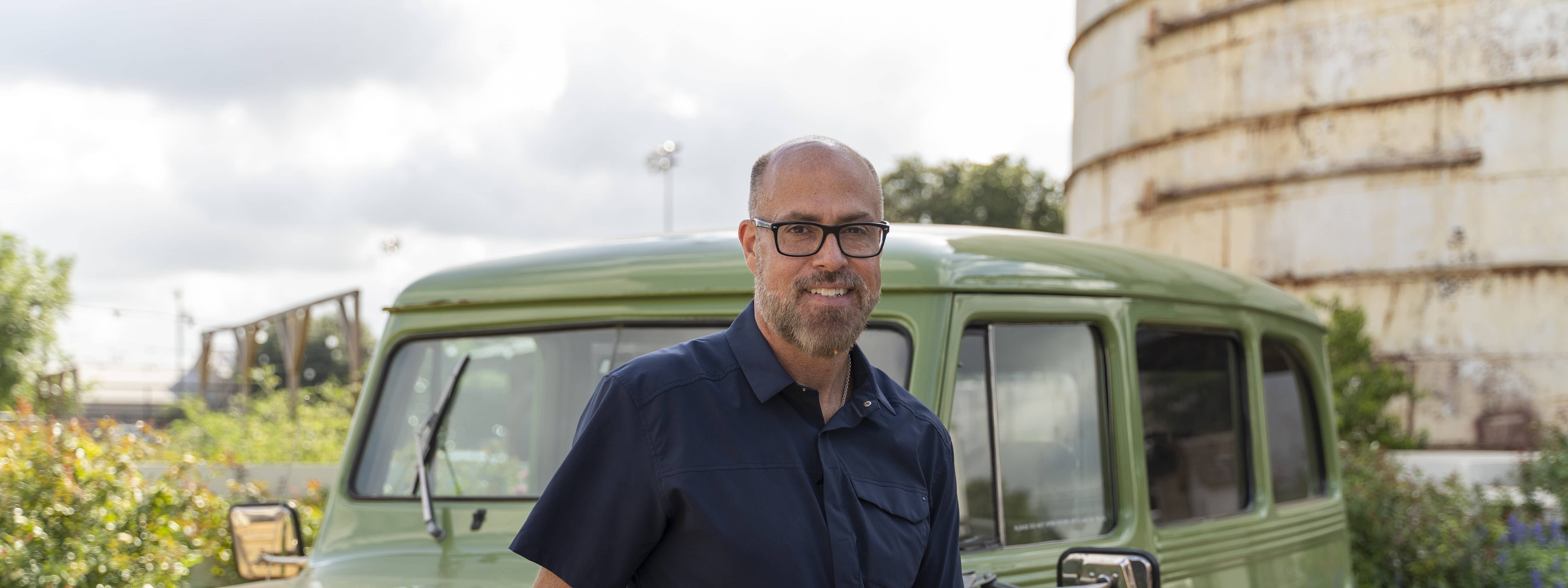 A man in glasses standing next to a green truck.