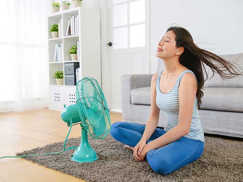 a woman sitting in front of a table fan