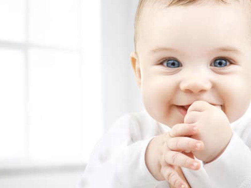 a baby smiling holding his thumb in mouth